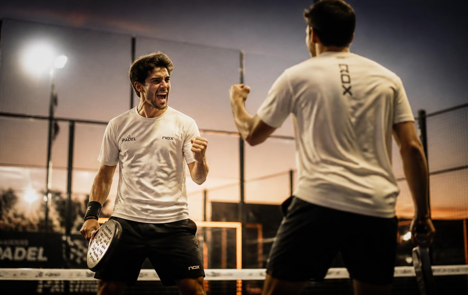 Two padel players celebrating a point on a floodlit glass court